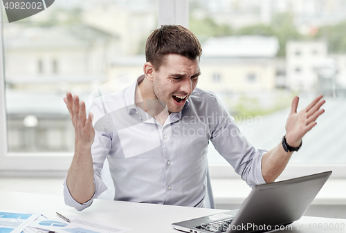 Image of angry businessman with laptop and papers in office