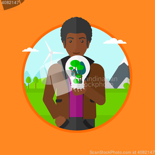 Image of Man holding light bulb with tree inside.