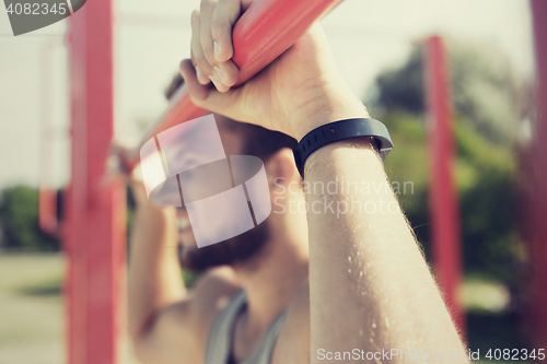 Image of young man exercising on horizontal bar outdoors