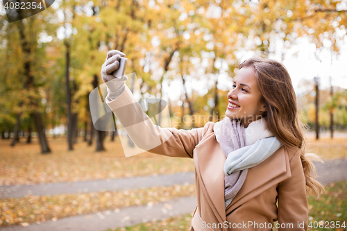 Image of woman taking selfie by smartphone in autumn park