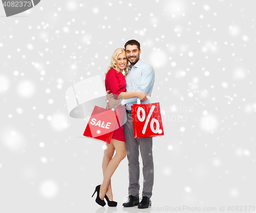 Image of happy couple with red shopping bags over snow