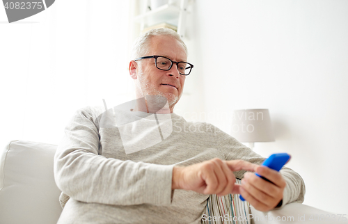 Image of happy senior man texting on smartphone at home