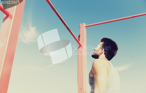 Image of young man exercising on horizontal bar outdoors