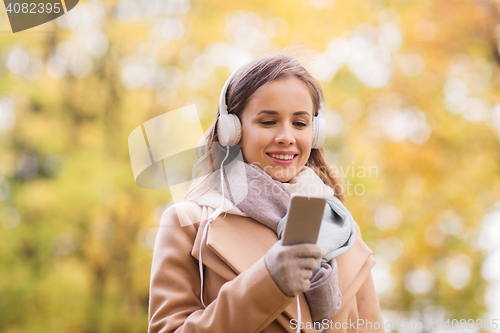 Image of woman with smartphone and earphones in autumn park