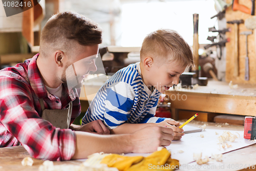 Image of happy father and son with blueprint at workshop