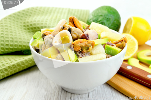 Image of Salad with seafood and lemon in bowl on light board