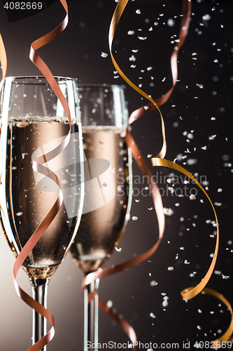 Image of Two champagne glasses, decorative ribbon on dark background with snowfall