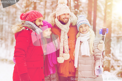 Image of smiling friends with smartphone in winter forest