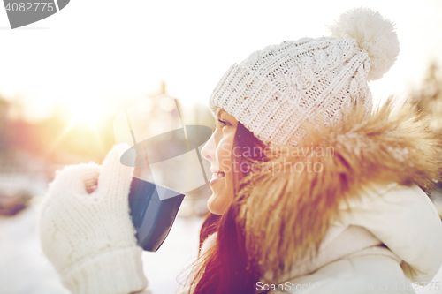 Image of happy young woman with tea cup outdoors in winter