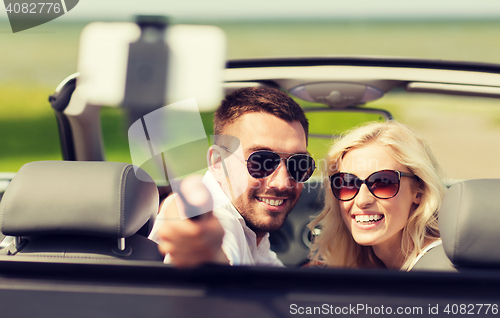 Image of happy couple in car taking selfie with smartphone