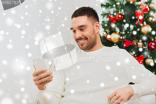 Image of smiling man with smartphone at home for christmas