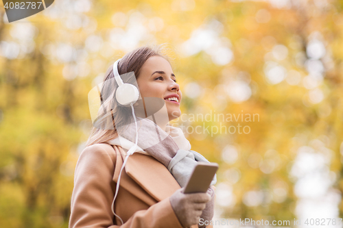 Image of woman with smartphone and earphones in autumn park