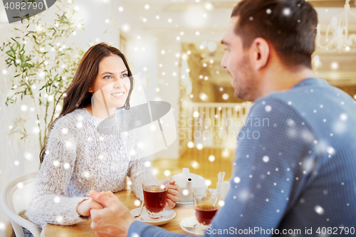 Image of happy couple with tea holding hands at restaurant