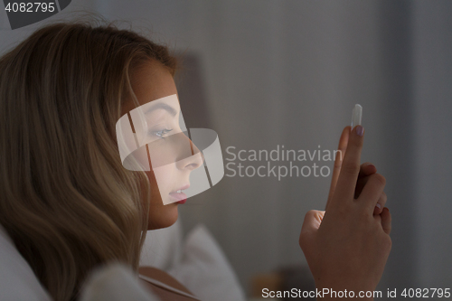 Image of young woman with smartphone in bed at night