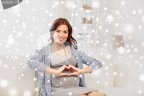 Image of happy pregnant woman making heart gesture at home