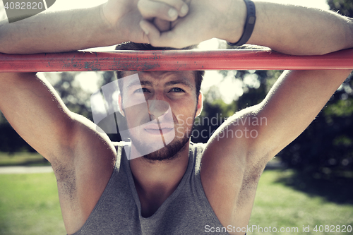 Image of young man exercising on horizontal bar outdoors