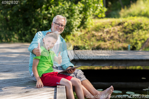 Image of grandfather and boy with tablet pc on river berth