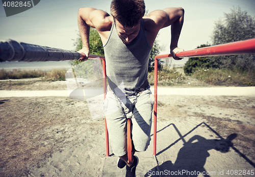 Image of young man exercising on parallel bars outdoors