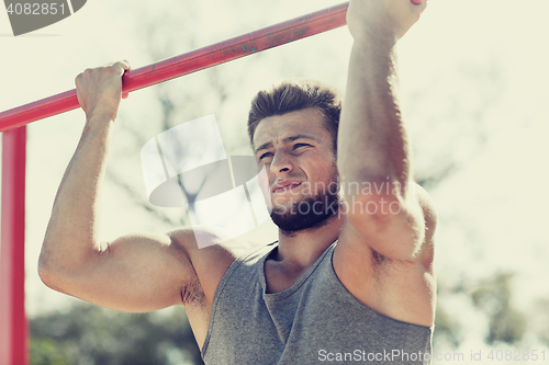 Image of young man exercising on horizontal bar outdoors