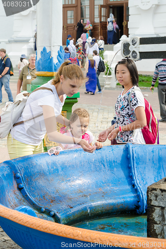 Image of Sergiev Posad - August 10, 2015: She visitor Holy Trinity St. Sergius Lavra washes the baby\'s face with holy water at the canopy over the cup with a cross