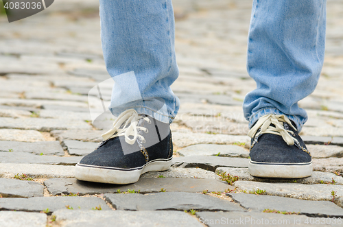 Image of Feet dressed in blue jeans and sneakers man closeup on stone pavement