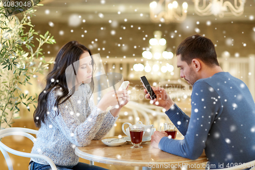 Image of couple with smartphones drinking tea at cafe