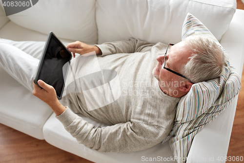 Image of senior man with tablet pc lying on sofa at home