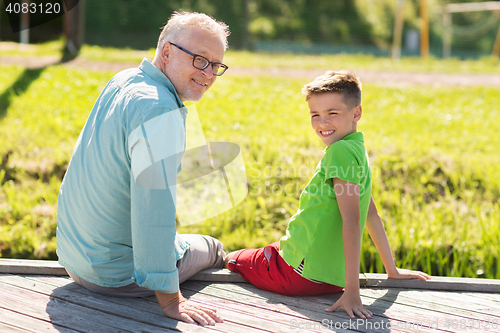 Image of grandfather and grandson sitting on river berth