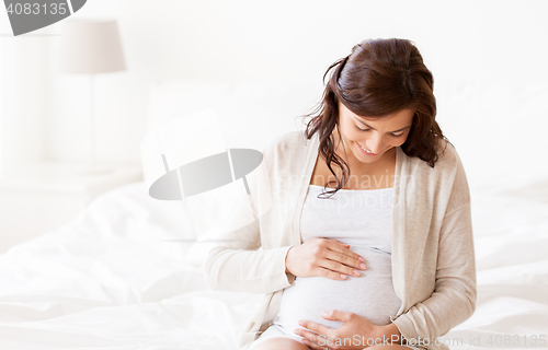 Image of happy pregnant woman sitting on bed at home