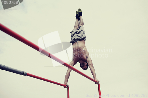 Image of young man exercising on parallel bars outdoors