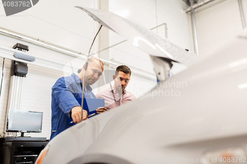 Image of auto mechanic with clipboard and man at car shop