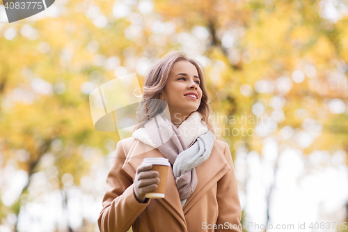 Image of happy young woman drinking coffee in autumn park