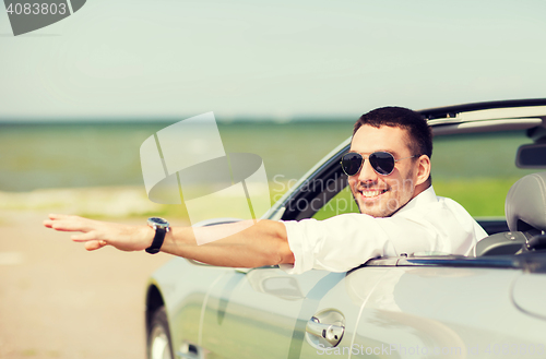 Image of happy man driving cabriolet car and waving hand