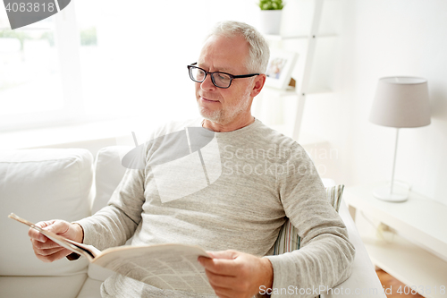 Image of senior man in glasses reading newspaper at home