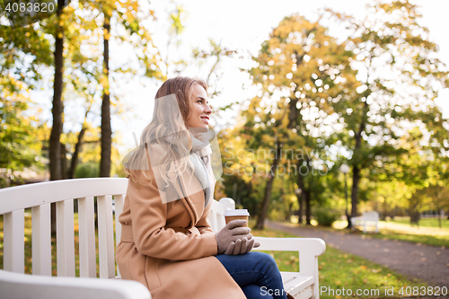 Image of happy young woman drinking coffee in autumn park