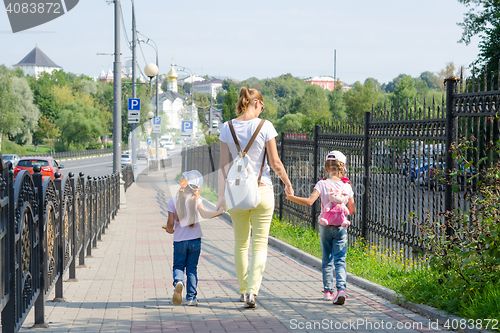 Image of Mother and two daughters are on the sidewalk along the road