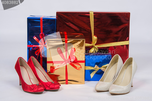 Image of Red and white female shoes with high heels, standing near boxes with gifts