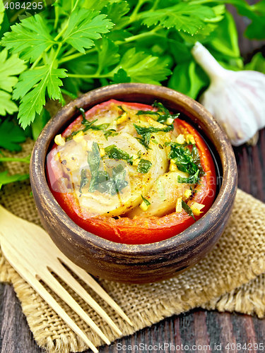 Image of Fish baked with tomato in clay bowl on dark board