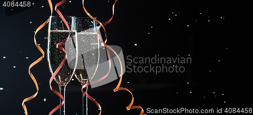 Image of Glasses of champagne decorated ribbons on black background with snowflakes