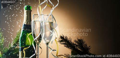 Image of Champagne bottle and glasses on background of Christmas tree branches