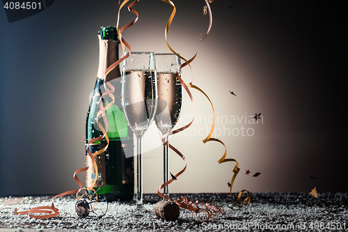 Image of Bottle of champagne, wineglasses with golden ribbons, snowflakes and serpentine