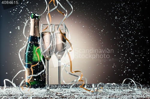 Image of Bottle, two champagne wineglasses with silver and golden ribbons, snowfall
