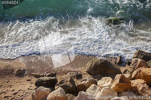 Image of Large stones on sandy beach and waves washing it