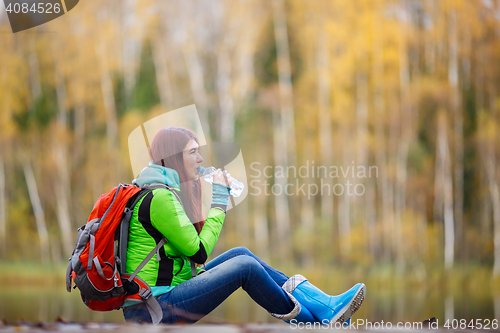 Image of Girl with long hair drinking water sitting among autumn trees