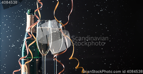 Image of Two champagne glasses and bottle on dark background with snowfall