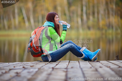 Image of Brunette drinks water sitting in autumn trees