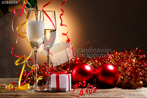 Image of Champagne pouring from bottle into glasses and Christmas decorations