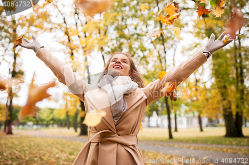 Image of happy woman having fun with leaves in autumn park