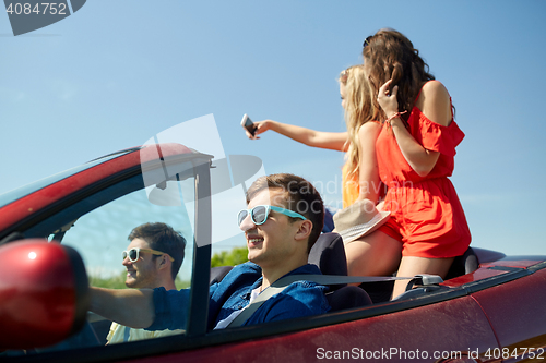 Image of friends driving in cabriolet car and taking selfie