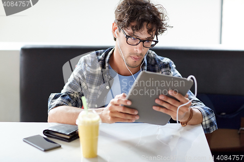 Image of man with tablet pc and earphones sitting at cafe